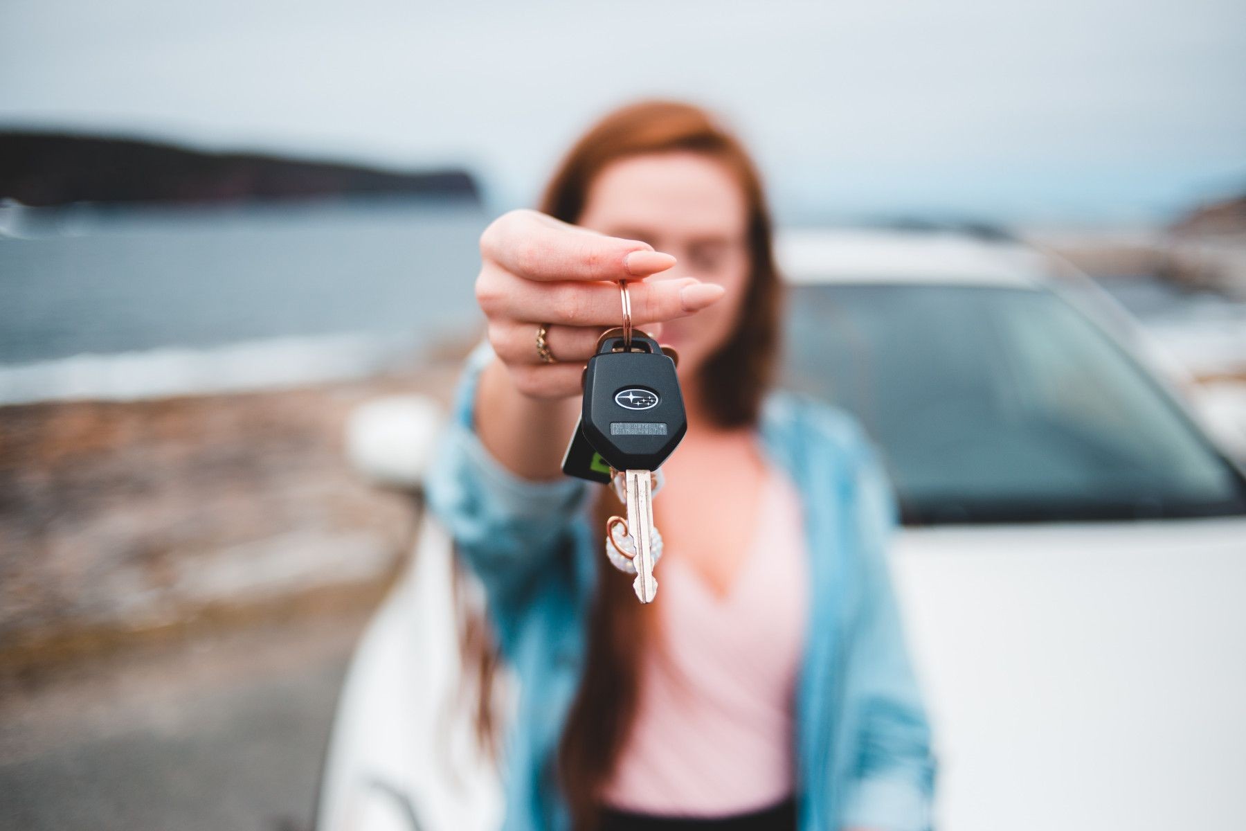 Woman holding car keys with a blurred background of a white car and ocean view.